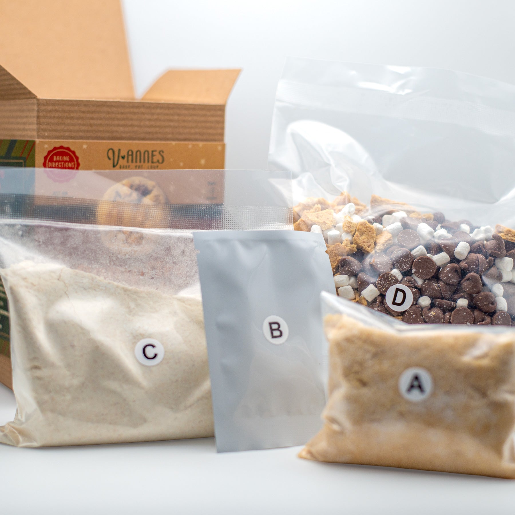 Four labeled pouches of ingredients or mix components arranged in front of an open cardboard box. The pouches are labeled A, B, C, and D.